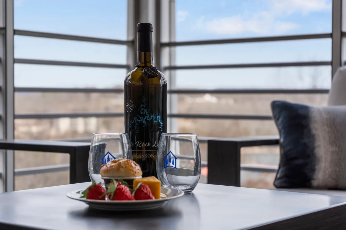 An intimate scene showing a wine bottle and glasses set on a table, with a plate of food and a glimpse of the view outside. The composition evokes cozy, romantic evenings spent dining or toasting to special moments at the condo.