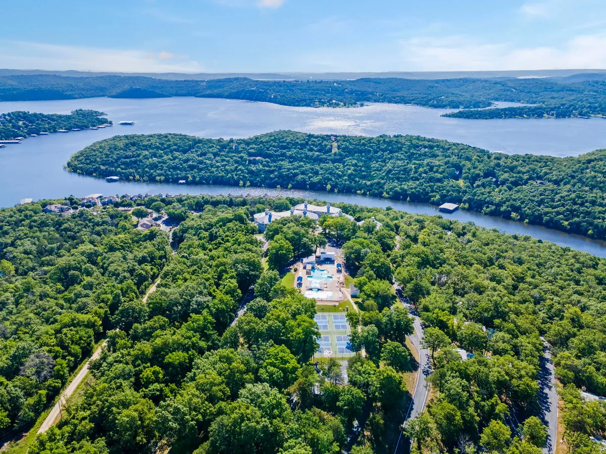 A scenic vista capturing the lake, a swimming pool, tennis courts, and lush surrounding trees. This panoramic exterior view illustrates the variety of outdoor recreational options available year-round, from swimming and tennis to hiking and lakeside relaxation.