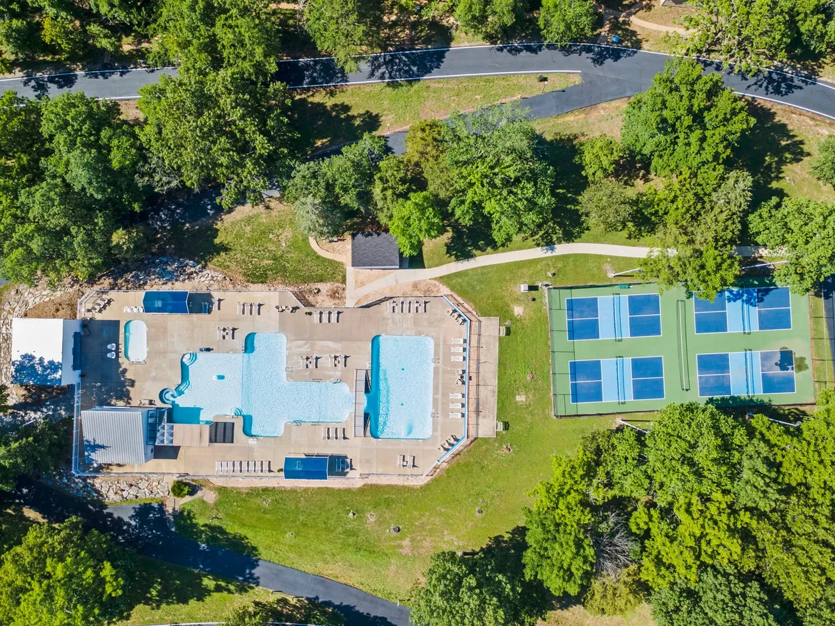 A broad exterior shot showcasing swimming pools, tennis courts, lounge chairs, and lush landscaped greenery. The layout emphasizes the variety of on-site activities available, from swimming and sunbathing to playing tennis, all set in an inviting resort landscape.