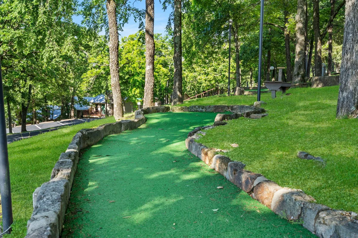 A playful mini-golf green winding through natural surroundings with stone borders and tall trees, inviting guests to engage in friendly competition or relax amidst nature. The scene is vibrant and welcoming, perfect for families or groups looking to enjoy outdoor amenities regardless of the season.