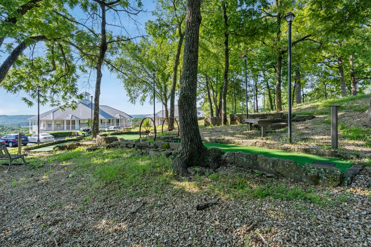 A playful mini-golf course nestled amid lush greenery, with stone pathways, classic park benches, and whimsical wagon wheel accents. The setting is inviting for guests of all ages, suggesting friendly competition and moments of laughter together outdoors.
