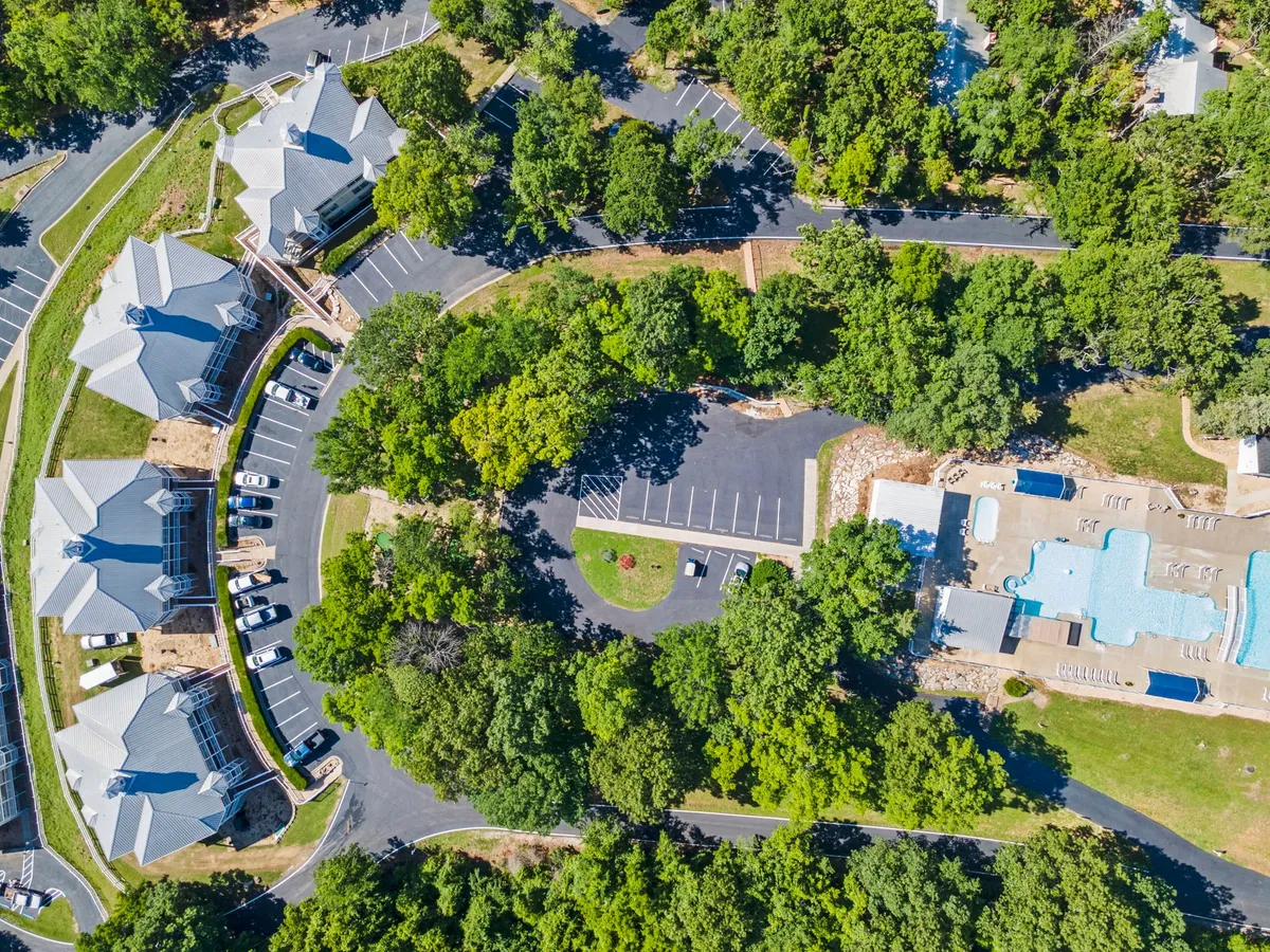 A bright, inviting outdoor pool surrounded by mature trees, with ample space for relaxation and activities like swimming or lounging. The pool area showcases the resort's seasonal outdoor amenities, while the sunny atmosphere makes it perfect for summer fun and water sports.