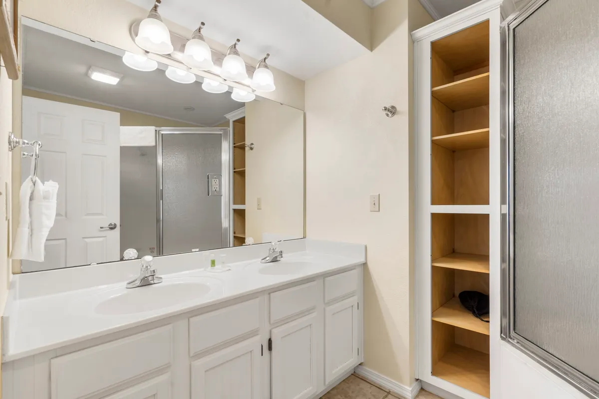 A well-appointed bathroom featuring a double sink, framed mirror, modern shower stall, and built-in shelves for storage. The space looks inviting and functional, ideal for unwinding after a day outdoors.