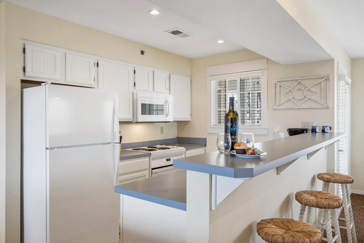 A modern kitchen with a central island, bar stools, a wine bottle, and a fruit platter set up for casual dining or entertaining. The layout flows into the living space, showcasing a seamless, open-concept design ideal for shared moments and planning adventures.